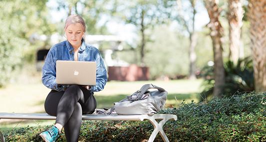 Student working on laptop sitting on a bench outside.